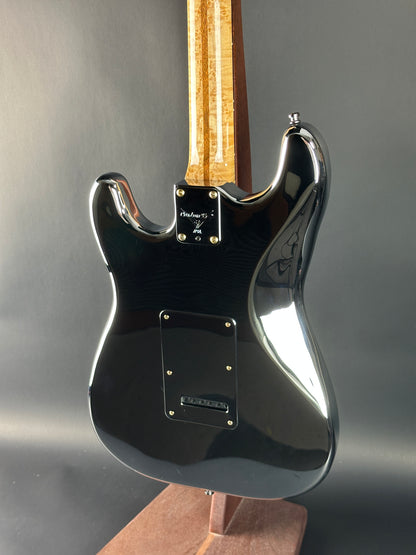 Close-up of a black electric guitar with a wooden neck on a gray background
