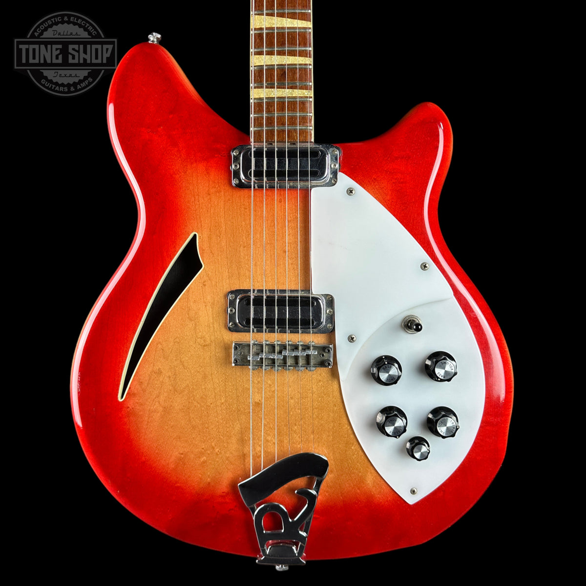 A double-cutaway electric guitar with a red and orange sunburst finish, featuring a white pickguard, chrome hardware, and a black f-hole overlay, shown against a solid black background.