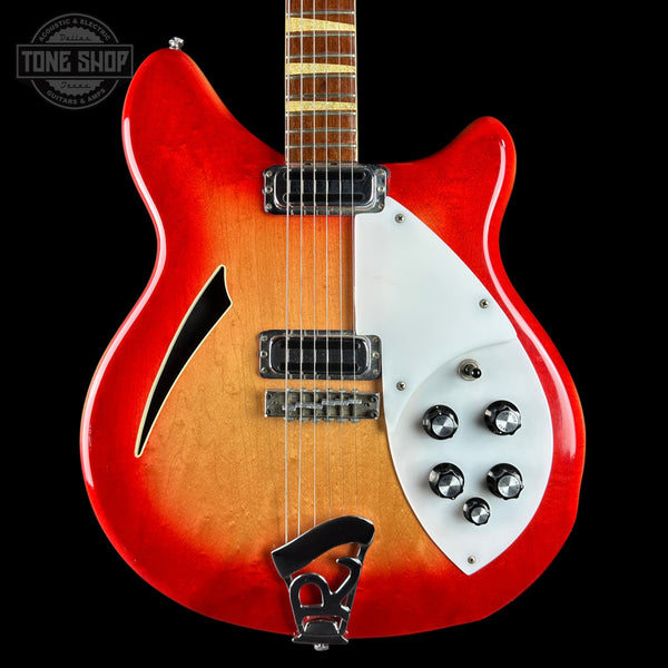 A double-cutaway electric guitar with a red and orange sunburst finish, featuring a white pickguard, chrome hardware, and a black f-hole overlay, shown against a solid black background.