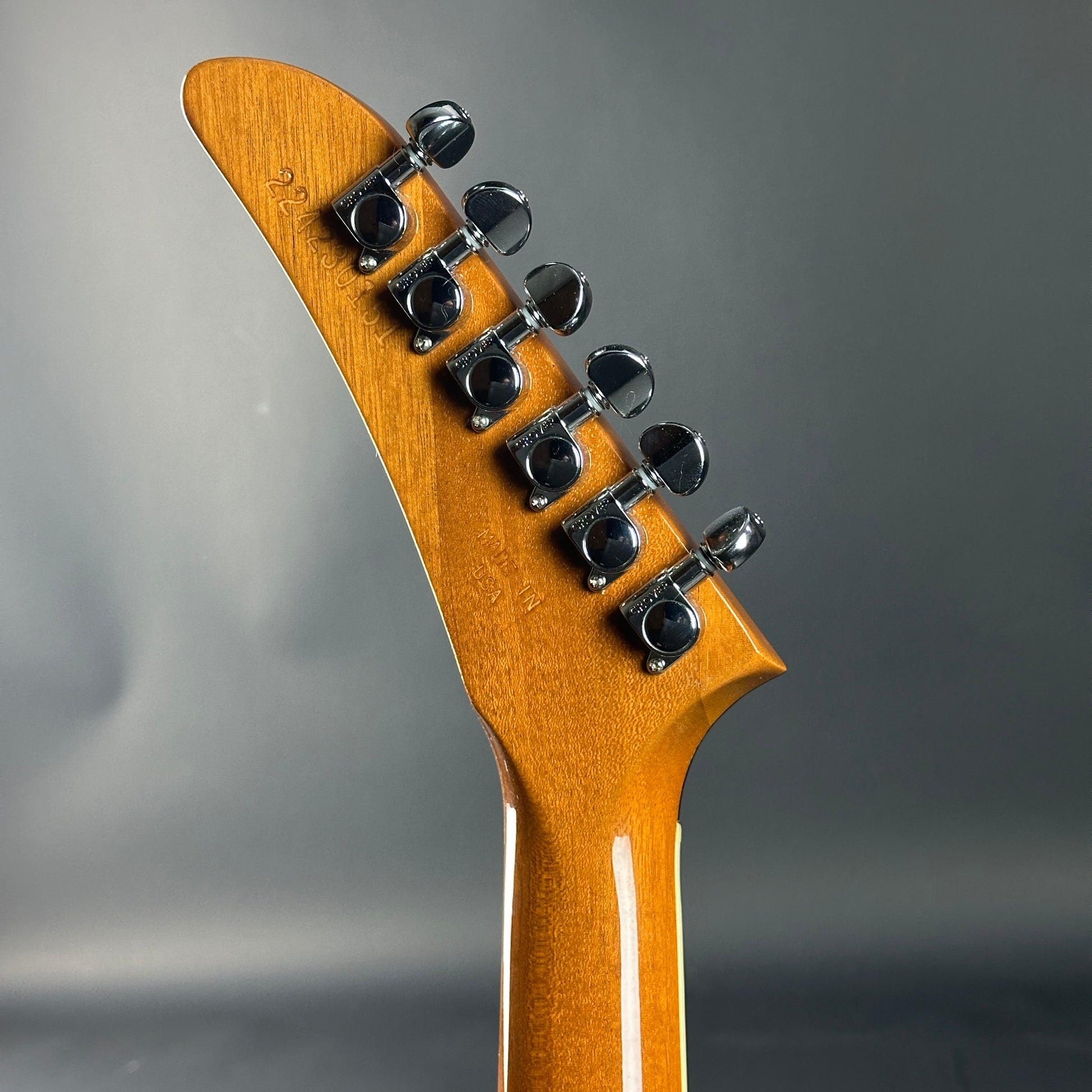 Close-up of a guitar headstock with tuning pegs on a gray background