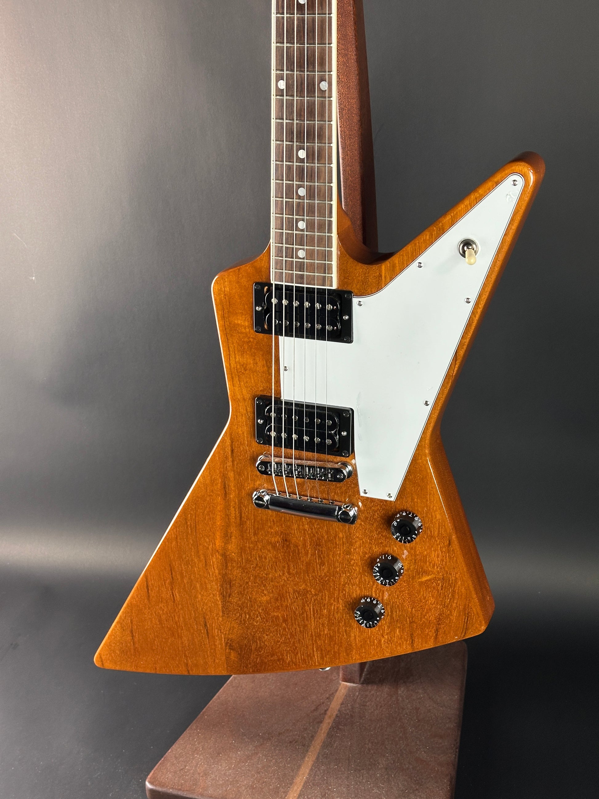 Wooden electric guitar with a white pickguard on a gray background