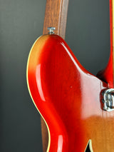 Close-up of the lower bout corner of an electric guitar body, showing a glossy sunburst finish that transitions from dark brown to warm amber-orange, with a light cream edge trim and part of the wooden neck visible.