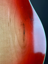 Close-up of a glossy wood surface with a warm reddish-brown gradient fading to light tan wood grain, bordered by a thin white stitched edge against a dark background.