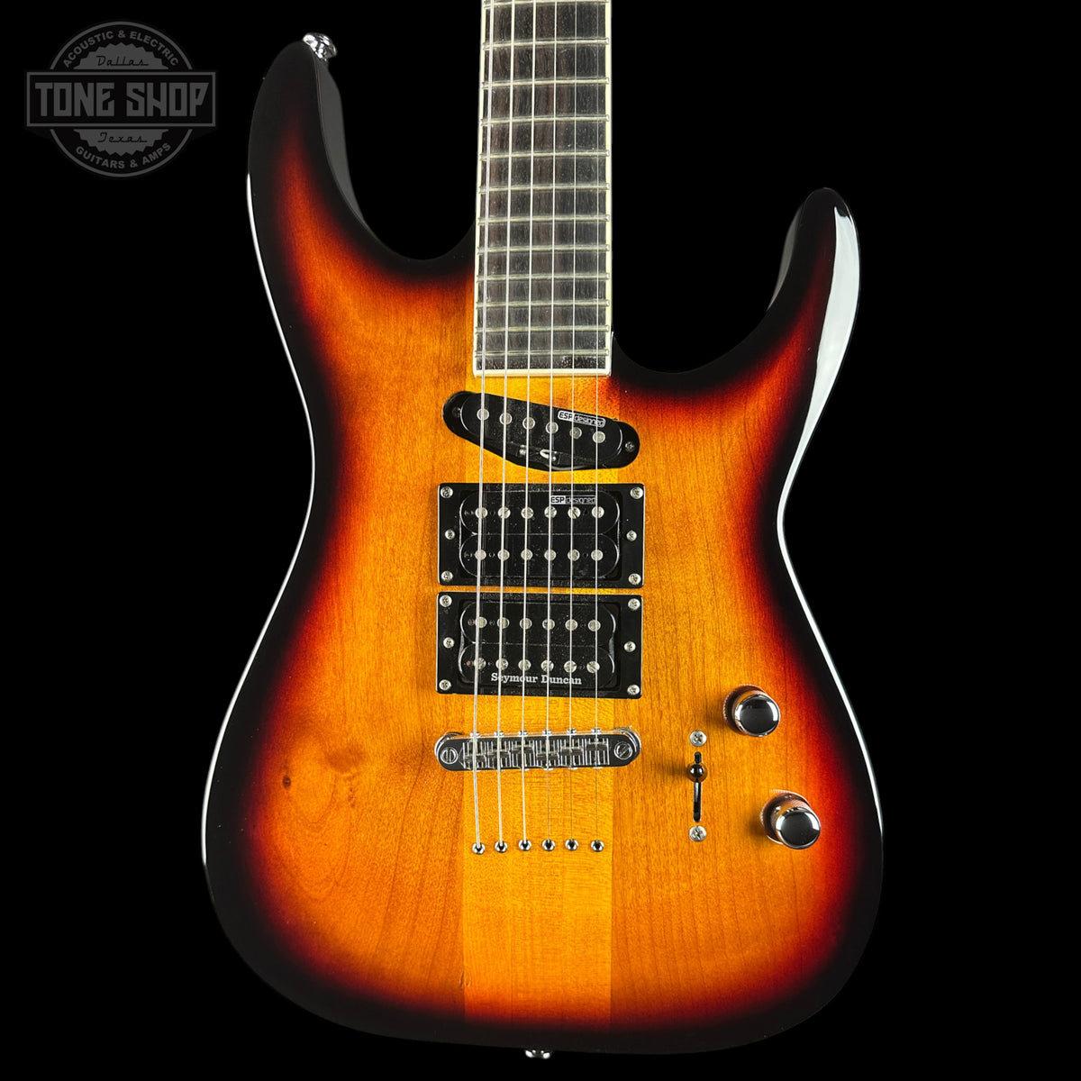 A double-cutaway electric guitar with a sunburst finish, featuring a bright orange center and dark brown to black edges. It has black hardware, a dark fretboard, and is photographed against a solid black background with a Tone Shop watermark in the top-left corner.