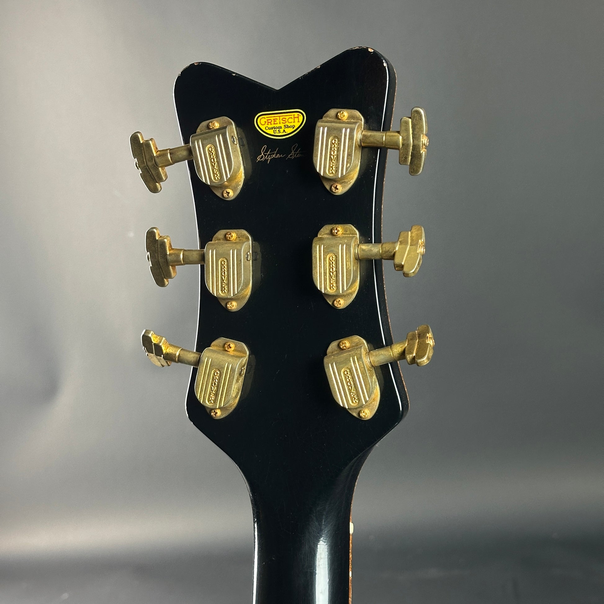Close-up of a guitar headstock with gold tuning pegs on a gray background