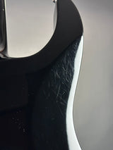 Close-up of a glossy black curved automotive body panel with visible scratches and scuffs on the surface, against a light gray background.