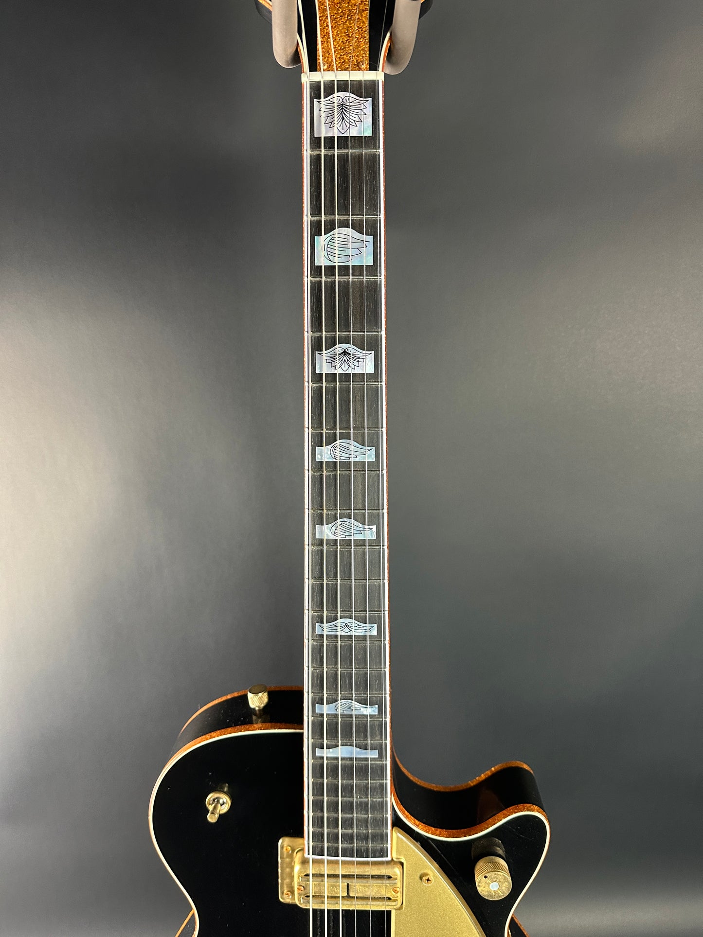 Close-up of a black electric guitar with gold hardware on a gray background