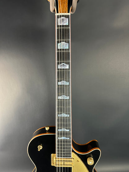 Close-up of a black electric guitar with gold hardware on a gray background