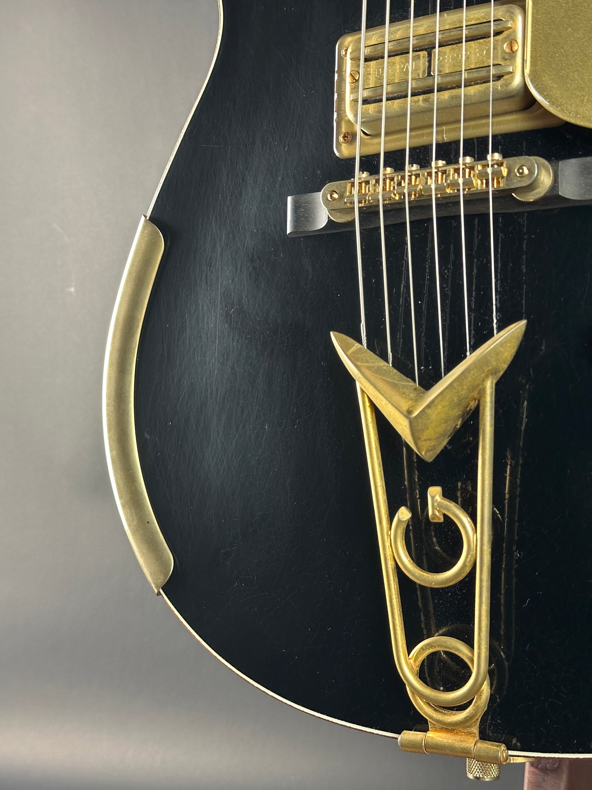 Close-up of a black guitar with gold hardware on a gray background