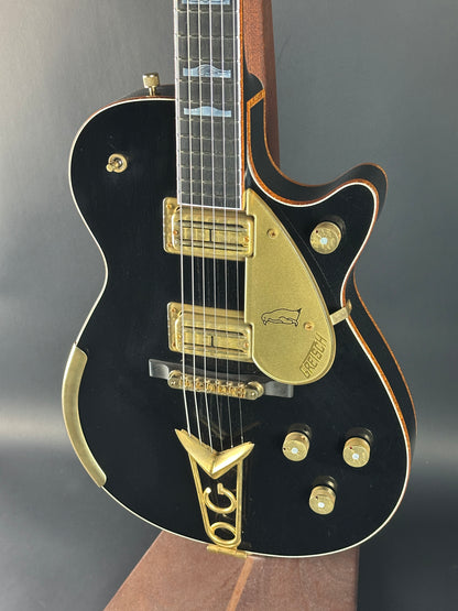 Black electric guitar with gold hardware on a gray background