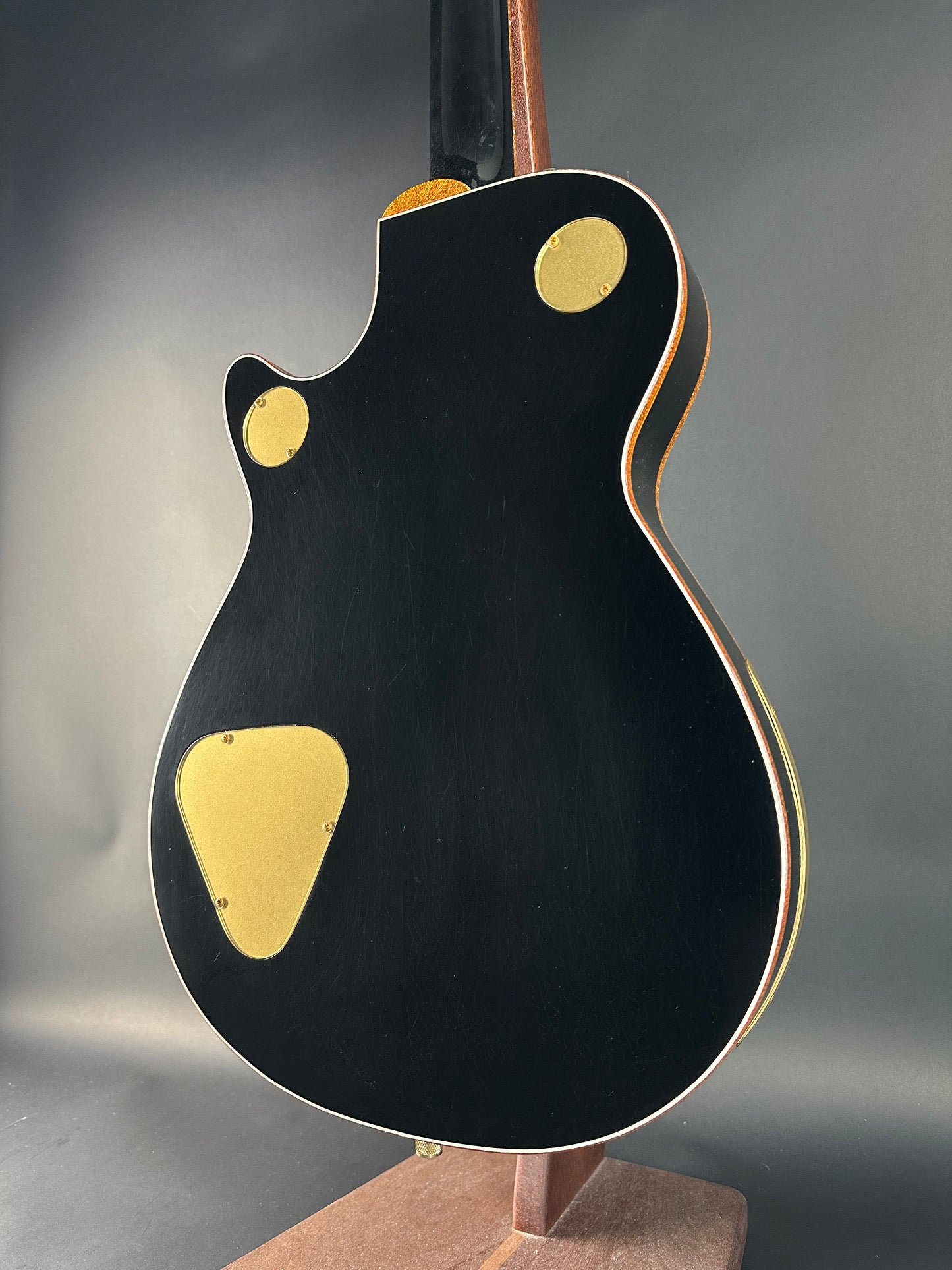 Close-up of a black electric guitar with gold pickguard on a gray background