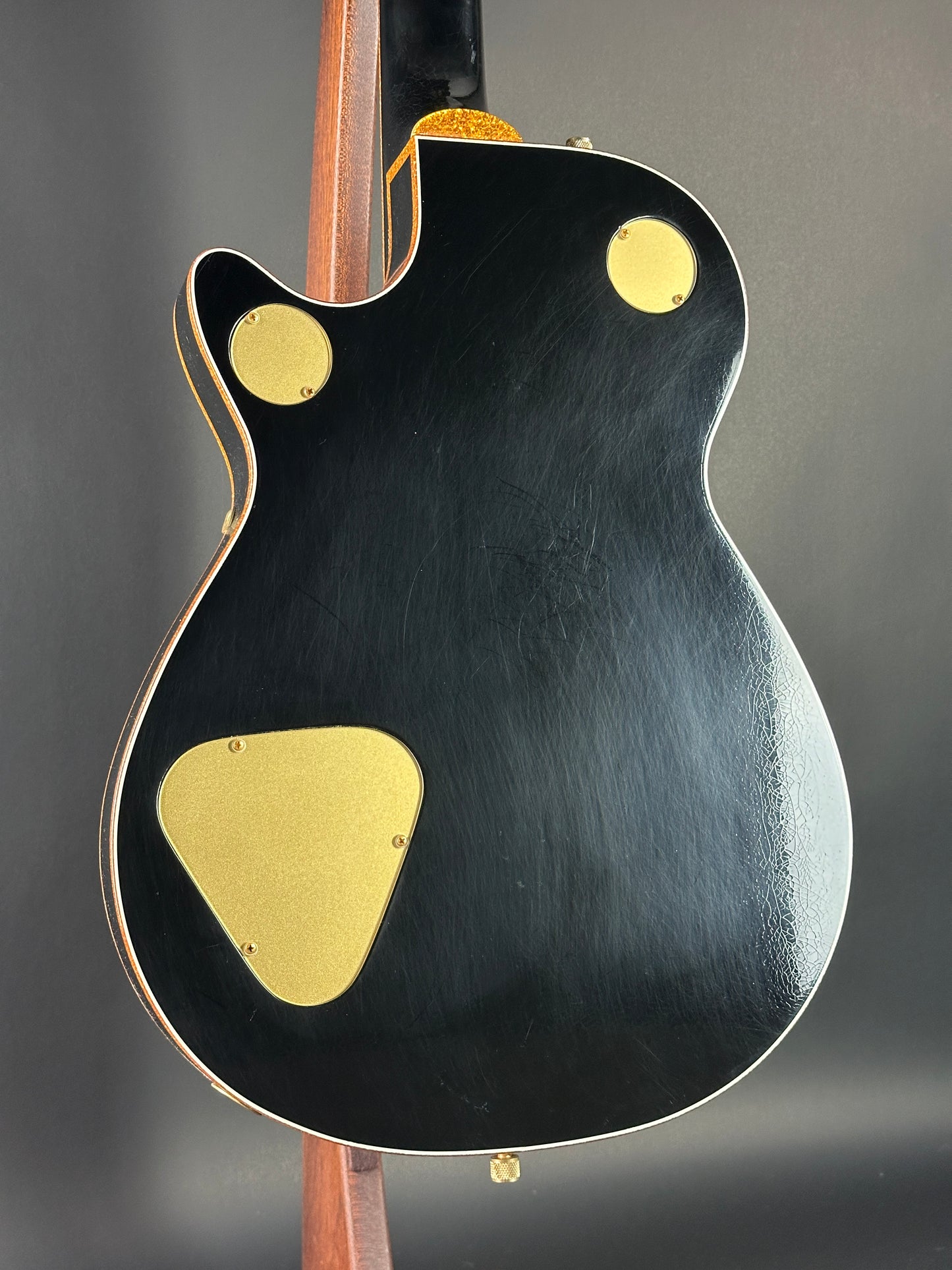 Close-up of a black electric guitar with gold pickguard on a dark background