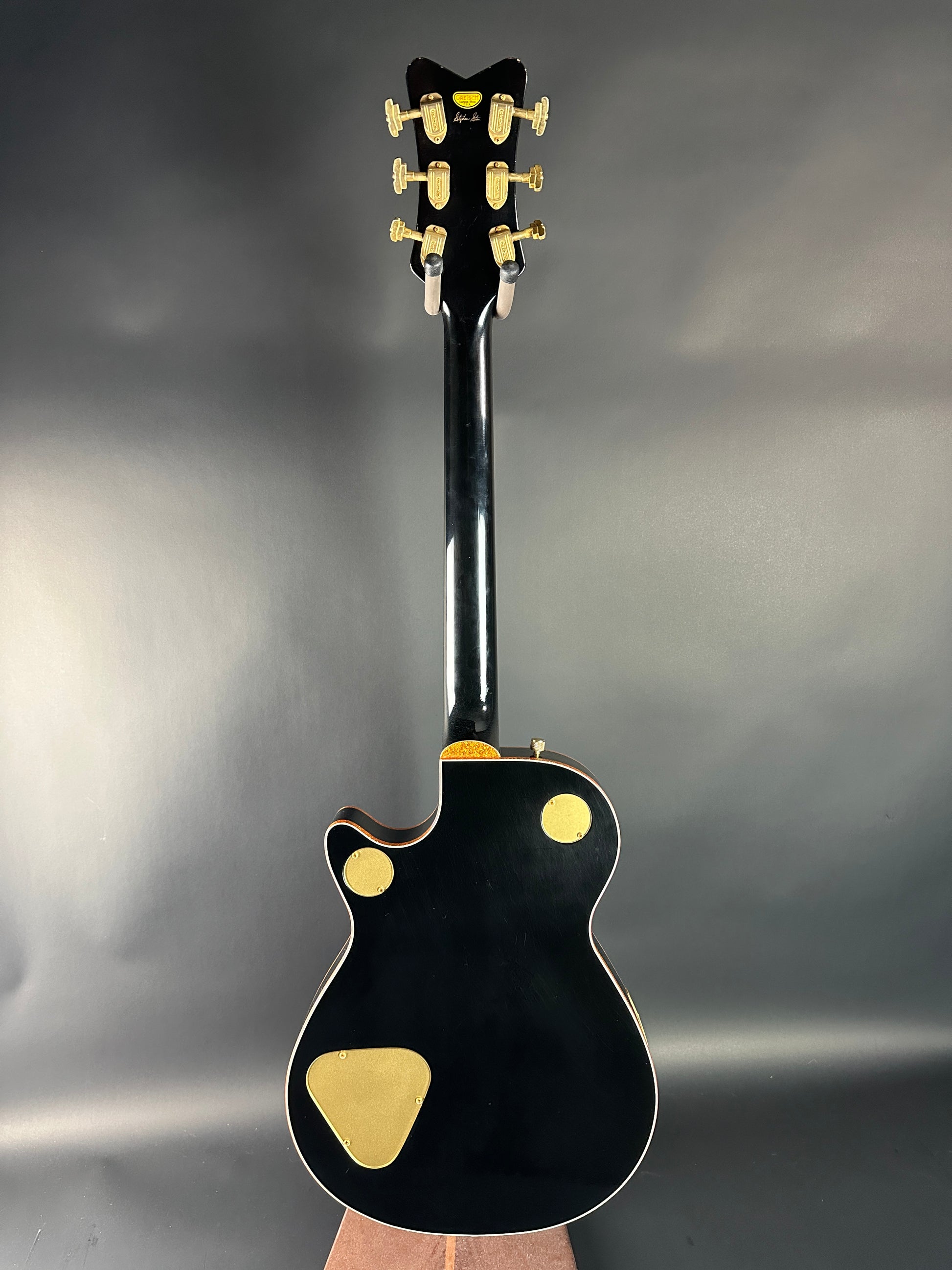 Black electric guitar with gold hardware on a gray background
