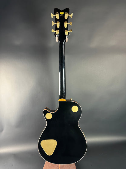 Black electric guitar with gold hardware on a gray background