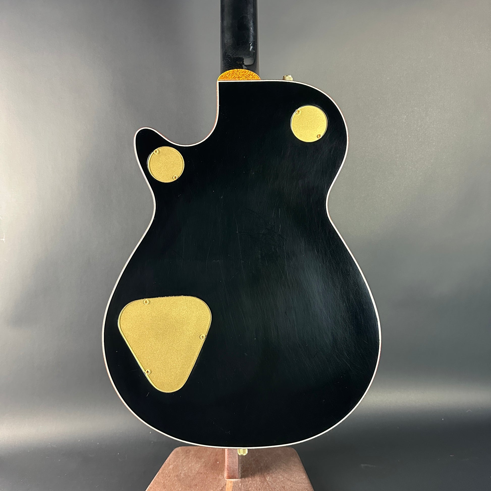 Black electric guitar with gold pickguard on a gray background