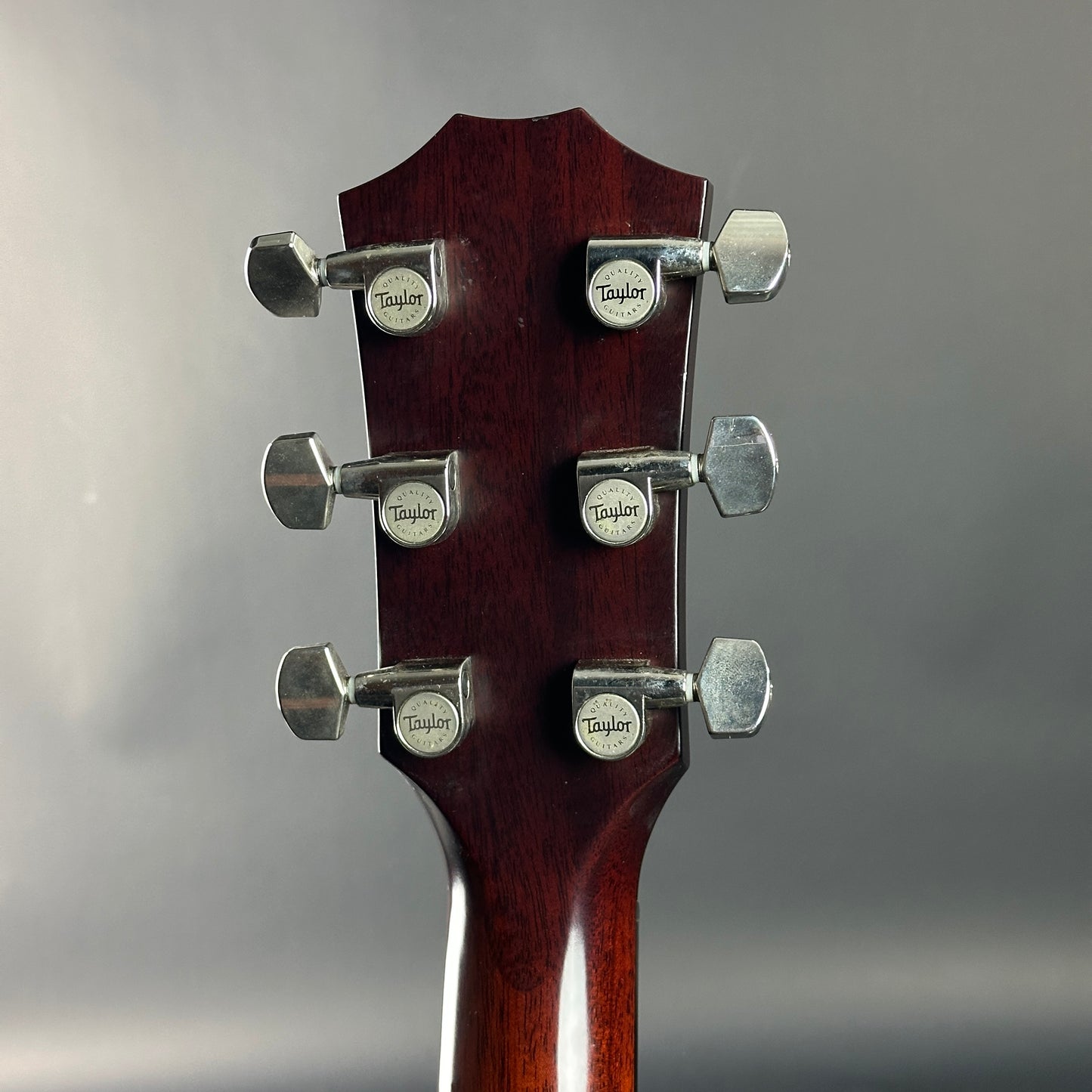 Close-up of a guitar headstock with tuning pegs on a gray background