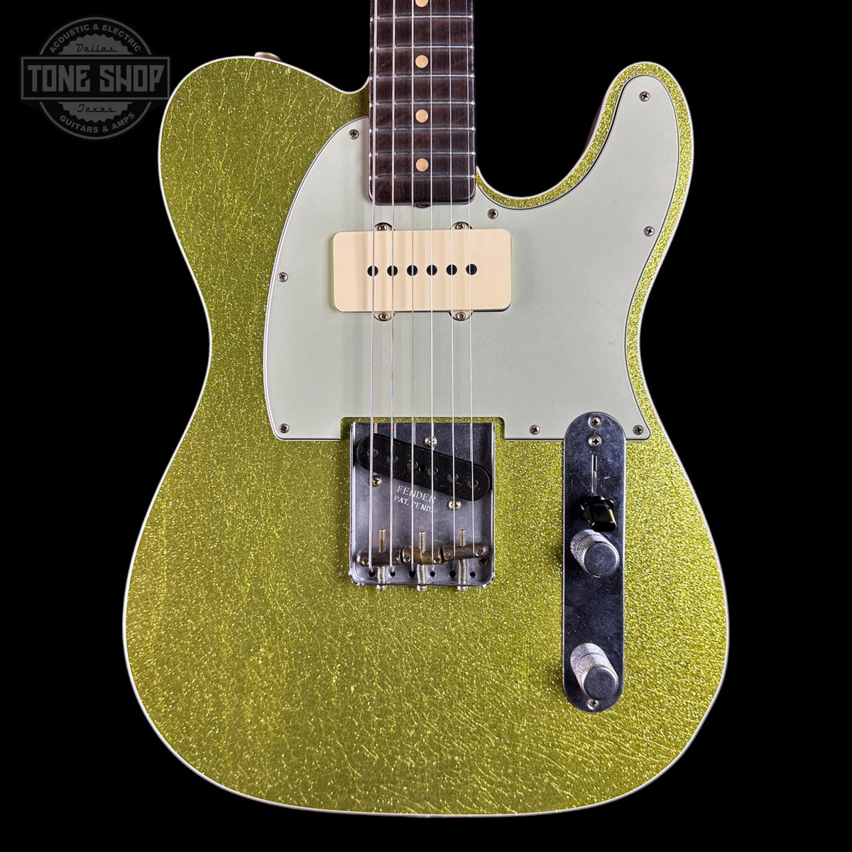 A close-up of a gold glitter electric guitar body with a cream pickguard, dual humbucker pickups, and chrome hardware, shown against a black background with a Tone Shop watermark in the top left.