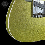 Close-up of a glittery gold electric guitar body with a black bridge and white edge trim, shown against a black background with a Tone Shop watermark.