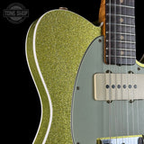 Close-up of an electric guitar body featuring a vibrant lime green glitter finish on the main body, a muted sage green pickguard, and a maple neck with a dark fretboard. A Tone Shop logo is visible in the top-left corner.