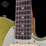 Close-up of an electric guitar showing the dark wood fretboard with gold dot inlays, a light green body, a gold glitter pickguard, and part of the neck against a black background. A Tone Shop watermark is visible in the top left corner.