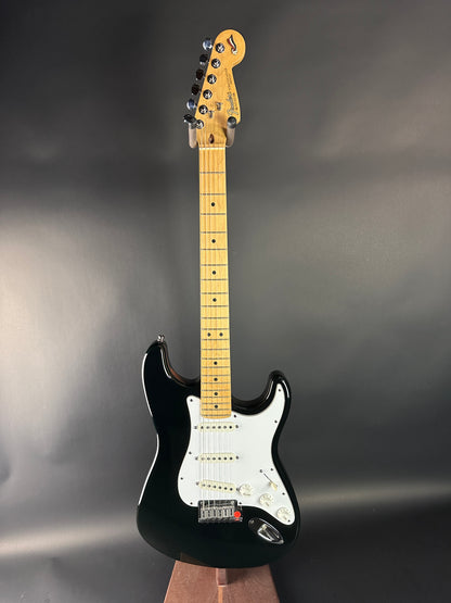 Electric guitar with a black body and white pickguard on a gray background