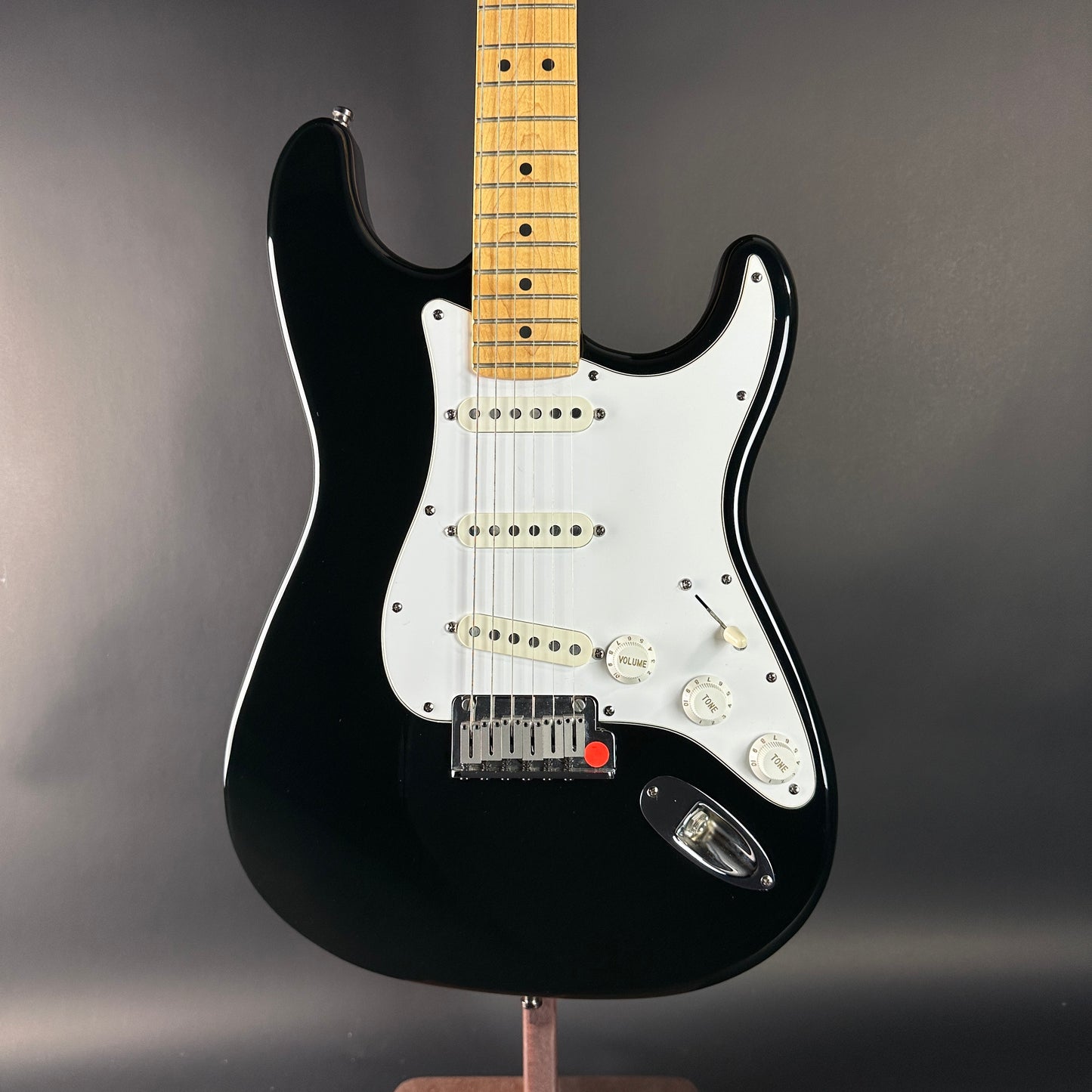 Black electric guitar with a wooden fretboard on a gray background