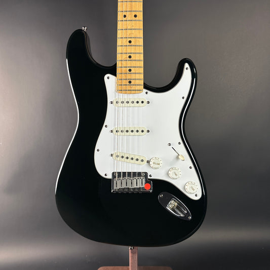 Black electric guitar with a wooden fretboard on a gray background
