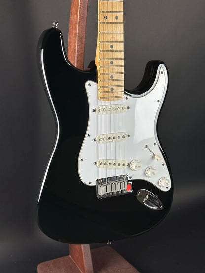 Black electric guitar with a white pickguard on a dark background