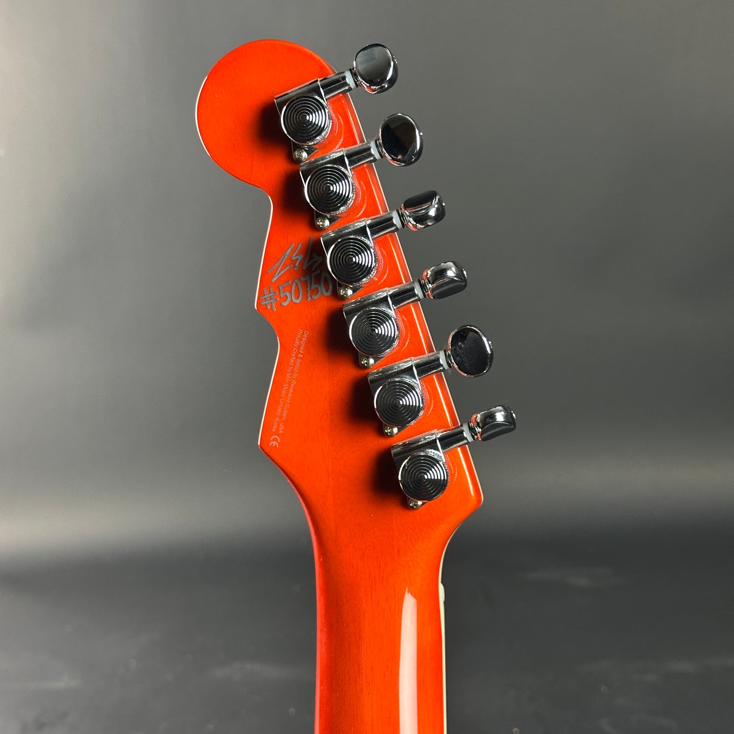 Close-up of an orange electric guitar headstock on a gray background