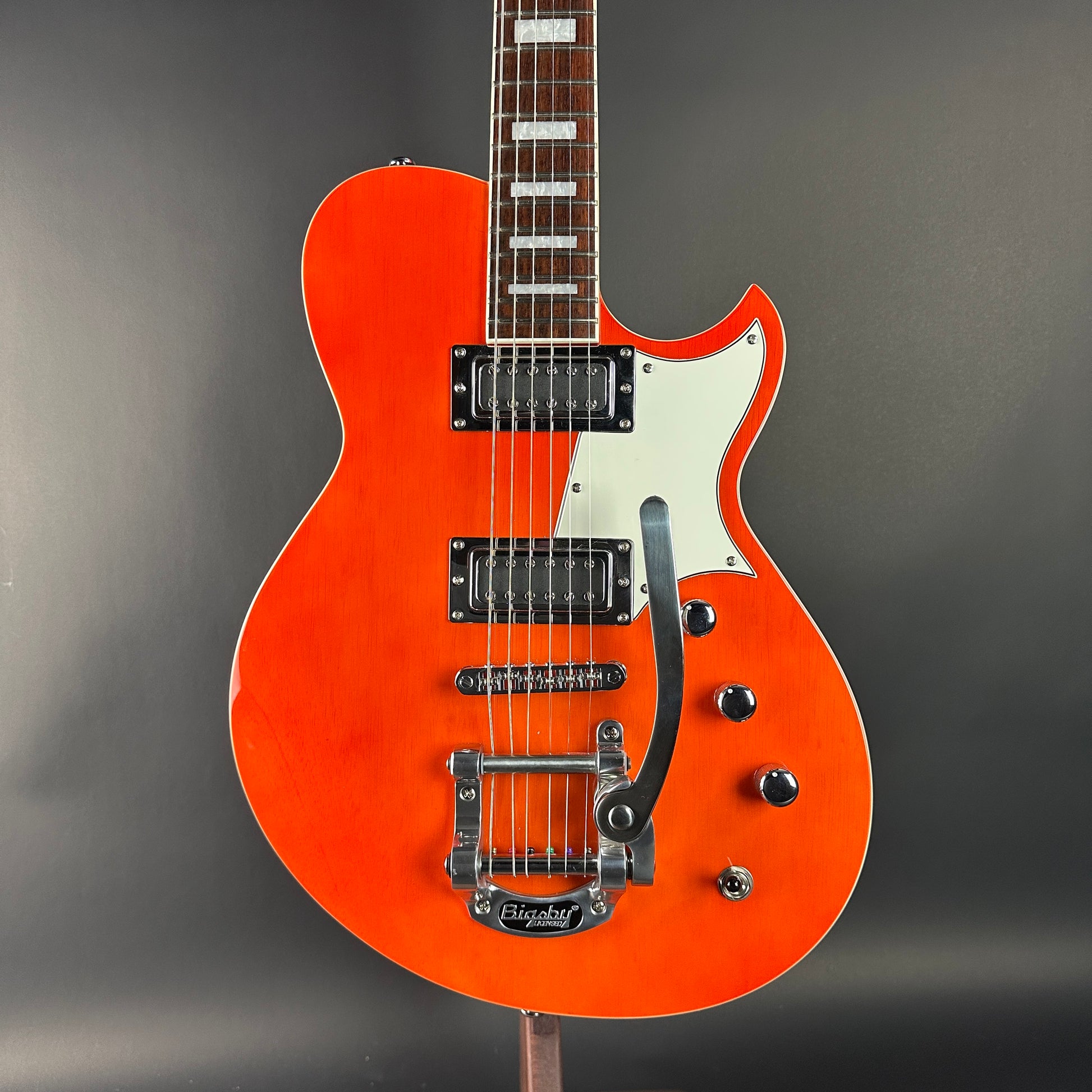 Orange electric guitar with a white pickguard on a gray background