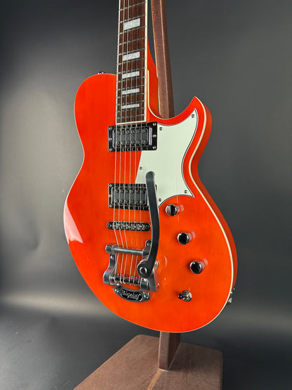Orange electric guitar with a white pickguard on a dark gray background