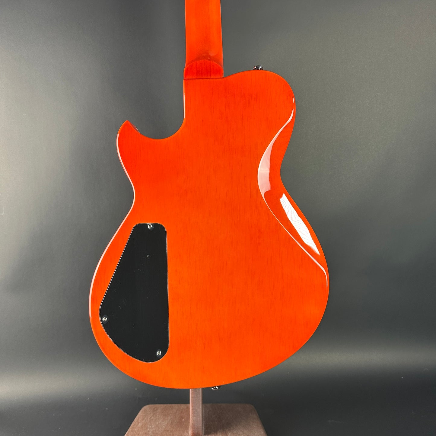 Orange electric guitar on a stand against a gray background