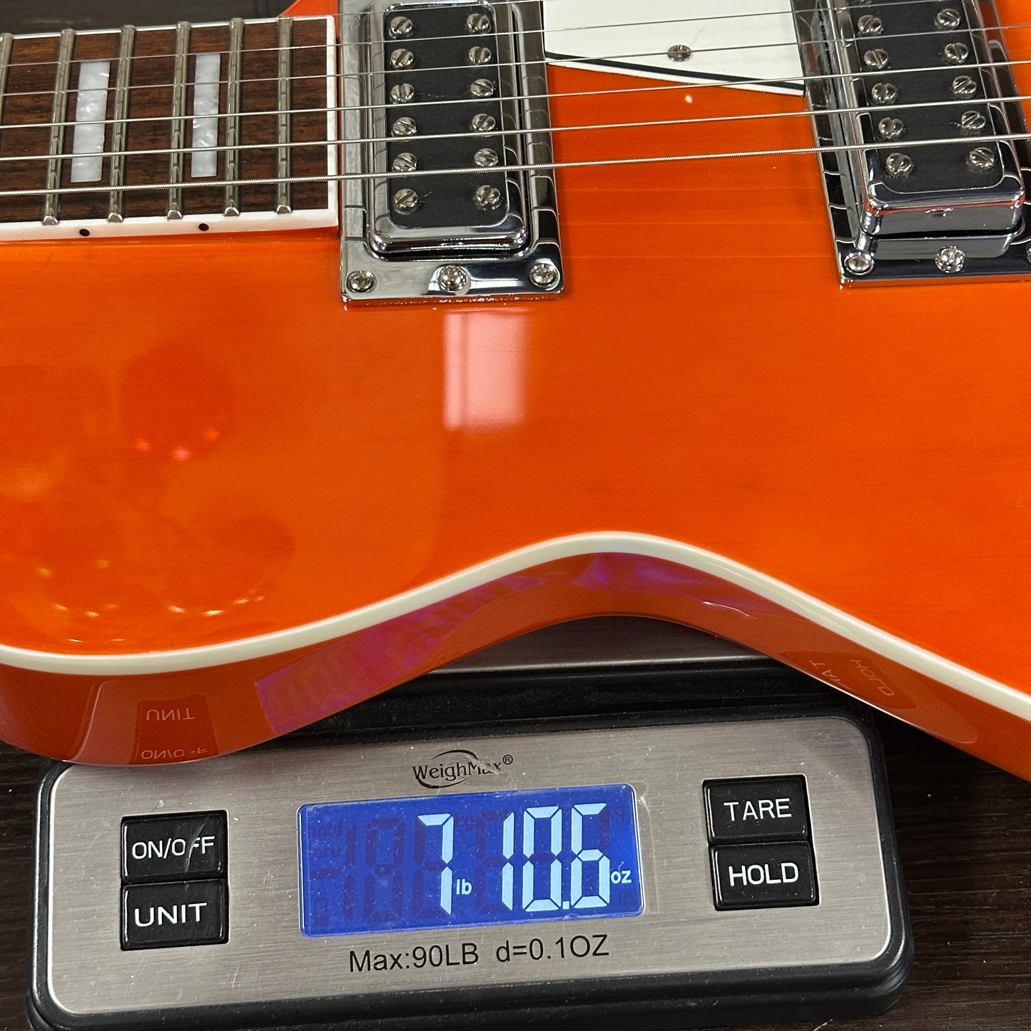 Orange electric guitar on a digital scale displaying weight.