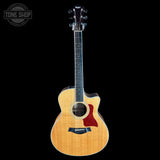 A Taylor acoustic-electric guitar with a natural wood finish and a red pickguard, shown against a solid black background with a Tone Shop watermark in the top-left corner.