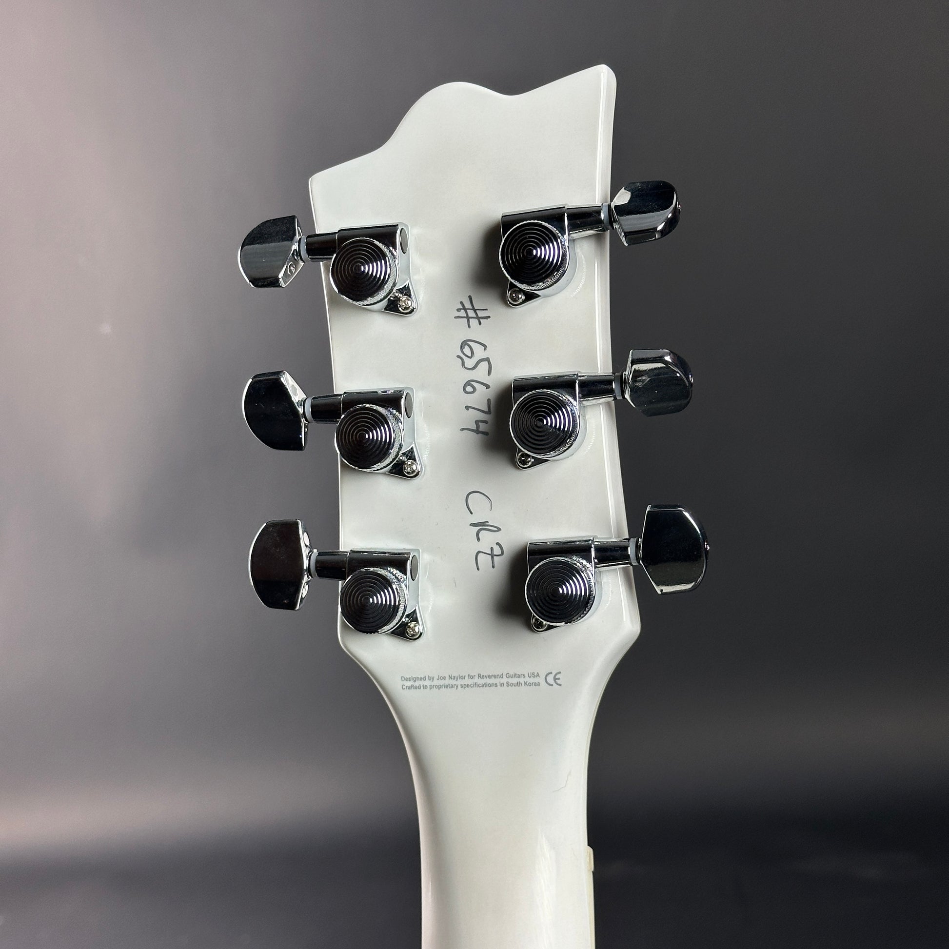 Close-up of a guitar headstock with tuning pegs on a gray background