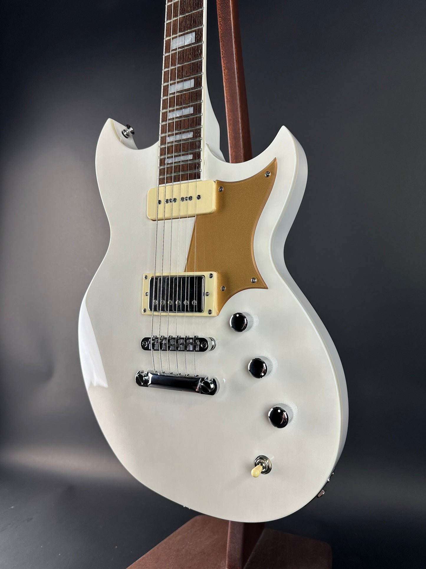White electric guitar with a gold pickguard on a dark background