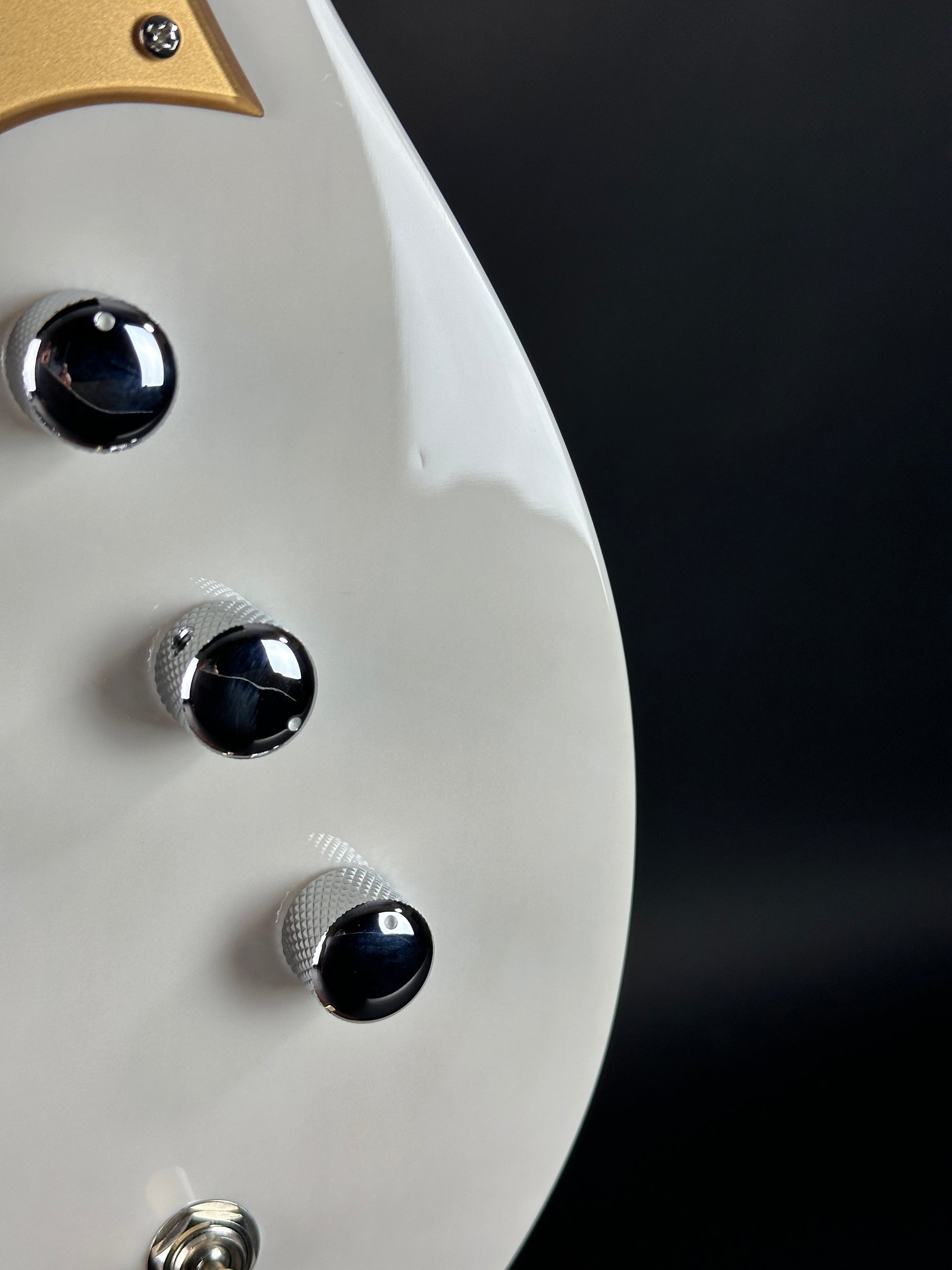 Close-up of a guitar headstock with control knobs against a dark background