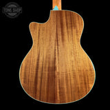 Close-up of the back of an acoustic guitar showing a rich wood grain finish, with a light blue binding edge visible against a solid black background.