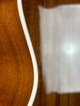 Close-up of a wooden guitar body showing a warm brown wood grain finish and a white binding edge.