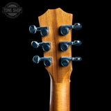 Close-up of a wooden guitar headstock with six black tuning pegs against a solid black background, featuring a Tone Shop watermark in the top left corner.