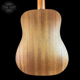 The back of a wooden acoustic guitar, showing a warm honey-brown wood grain finish, set against a solid black background with a Tone Shop watermark in the top left corner.