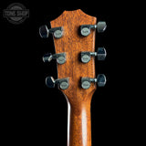 Close-up of the headstock of a Taylor acoustic guitar, showing six tuning pegs and the Taylor logo on each peg, set against a solid black background.