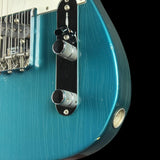 Close-up of a teal electric guitar with control knobs on a black background