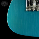 Close-up of a teal electric guitar with a visible brand logo in the corner.