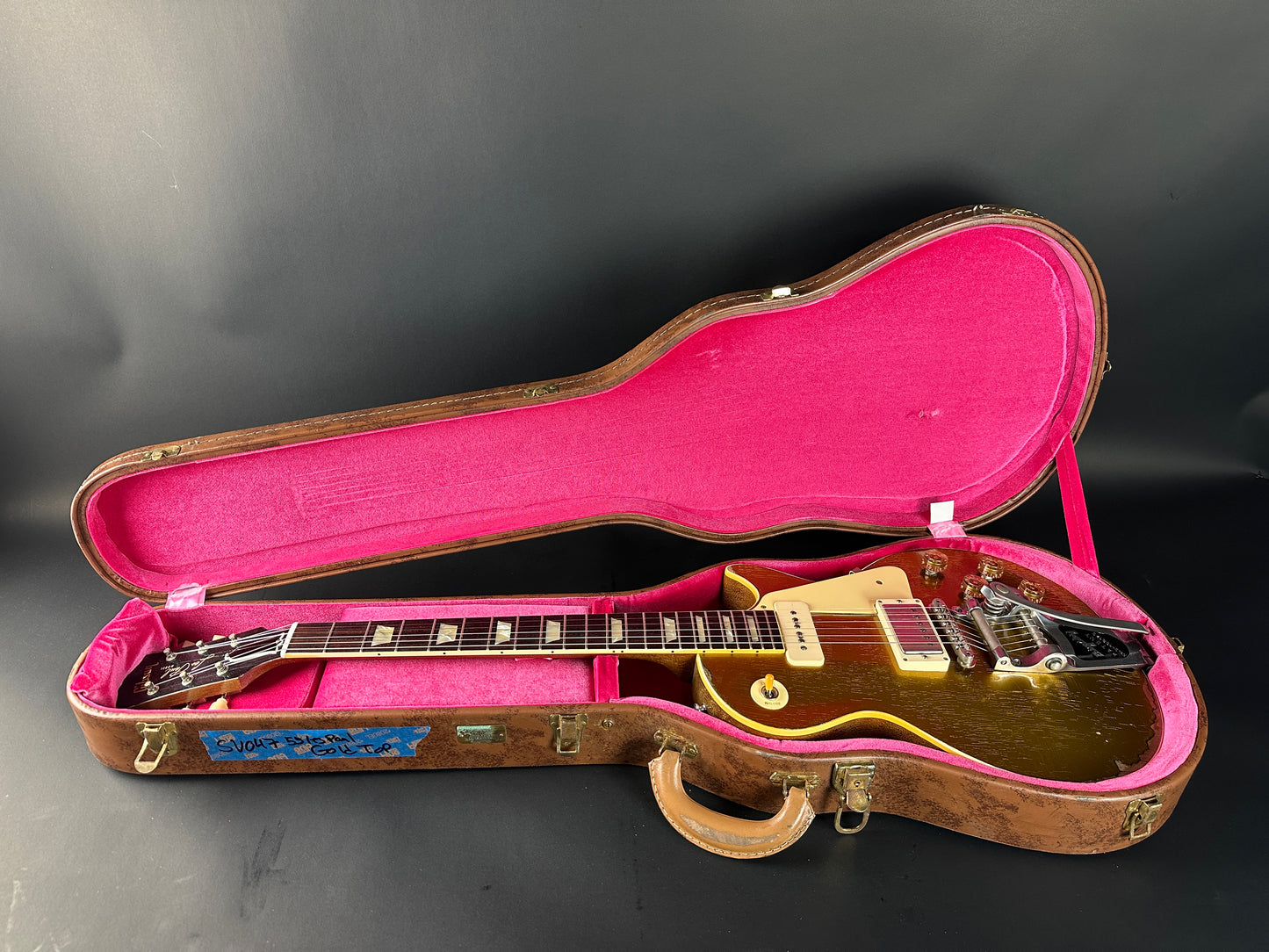 Gold electric guitar in a pink-lined case on a dark background