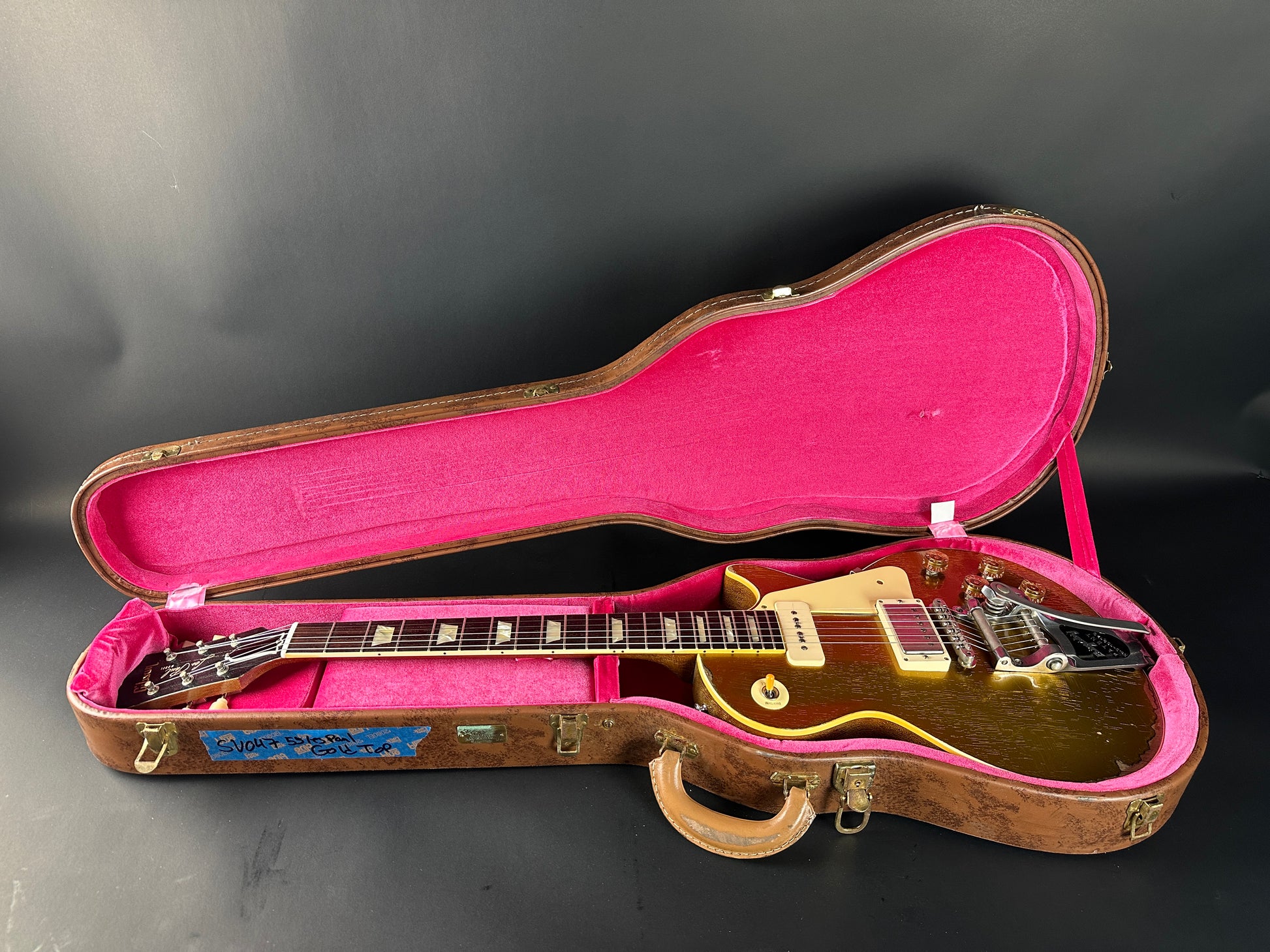 Gold electric guitar in a pink-lined case on a dark background