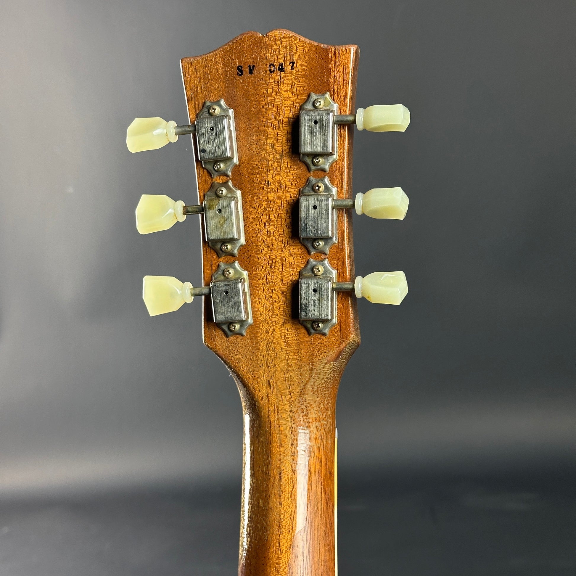 Close-up of a guitar headstock with tuning pegs on a gray background