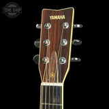 Close-up of a Yamaha acoustic guitar headstock, showing the dark wood grain, gold lettering, and silver tuning keys against a black background.