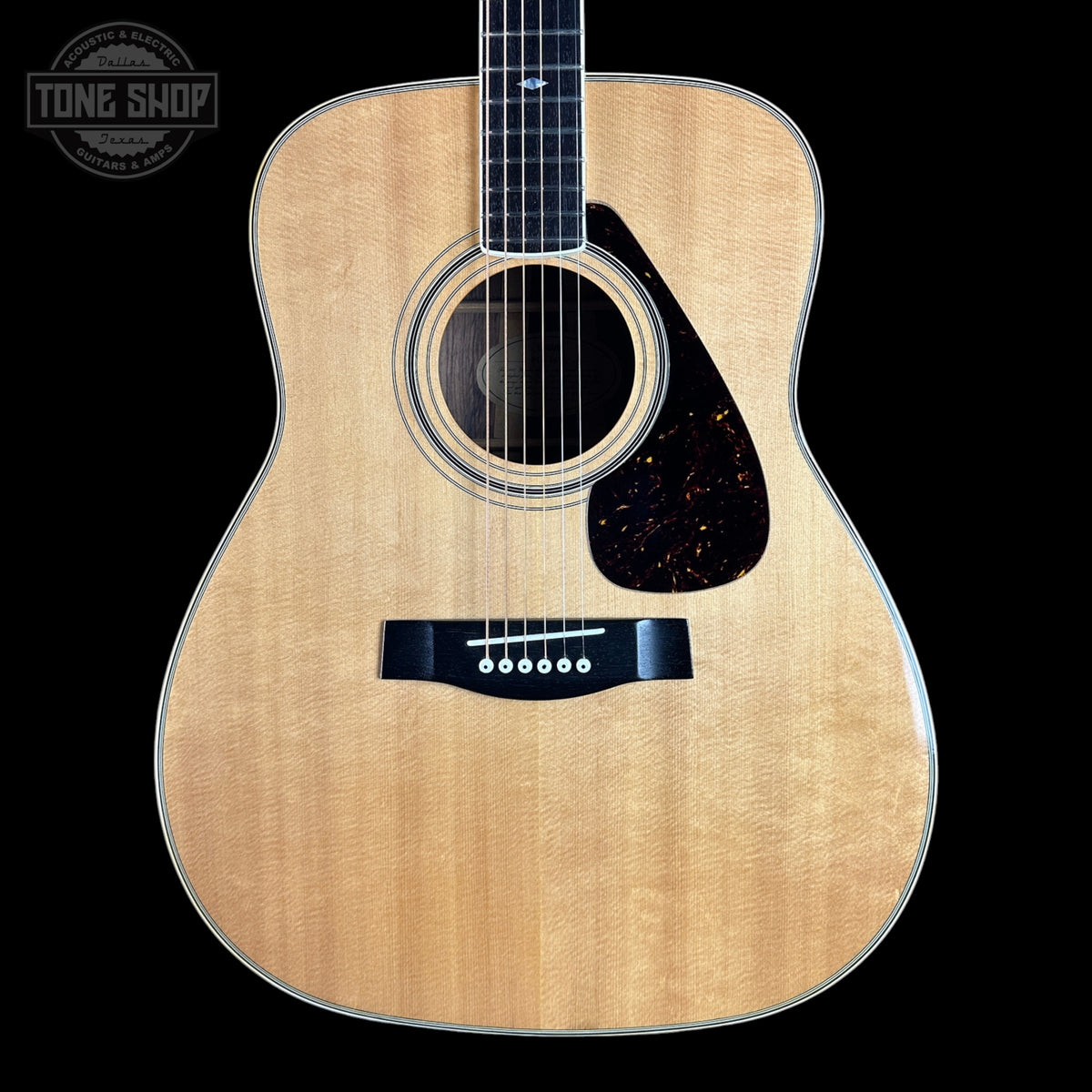 A natural wood acoustic guitar shown from the front against a solid black background, with a Tone Shop watermark in the upper left corner.