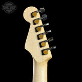 Close-up of a guitar headstock with tuning pegs on a black background, featuring the Tone Shop logo.